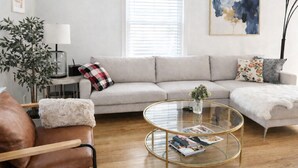 A modern living room with a beige sofa, a glass coffee table, a brown leather armchair, and a floor lamp.