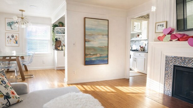 A spacious living room with hardwood flooring, a white fireplace, and a dining area with a glass table and chairs.