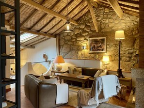 A cozy living room with a stone wall, wooden beams, a leather sofa, and a table with a lamp.