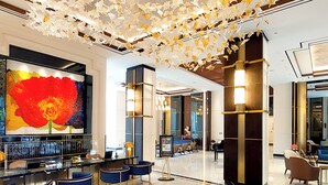 Um lobby moderno com piso de mármore, uma grande pintura abstrata e um teto com detalhes em forma de folhas.