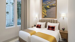 Quarto de hotel com uma cama grande, duas mesas de cabeceira, uma janela com cortinas e um quadro na parede.