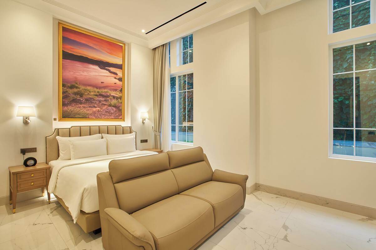 A hotel room with a large bed, a sofa, a nightstand, and a painting of a sunset over a beach.