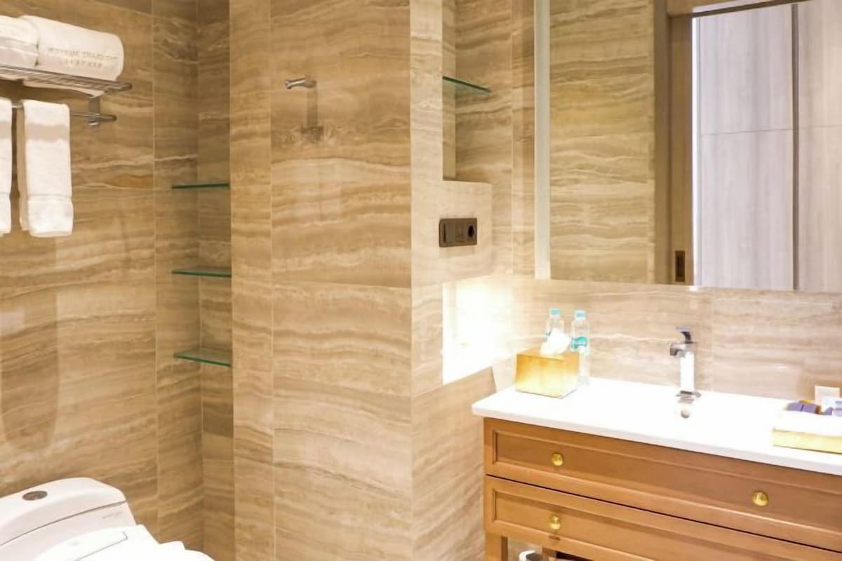 A bathroom with a marble wall, a glass shower enclosure, a white sink, and a wooden vanity.