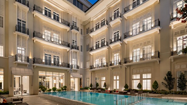Um hotel com vários andares, piscina central, varandas e interior bem iluminado.
