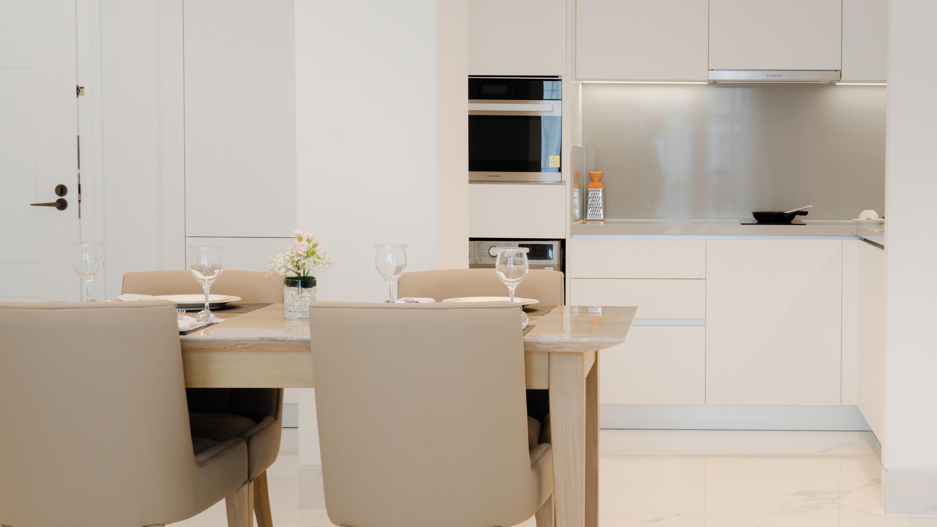 A modern kitchen with white cabinets, a stainless steel range hood, and a dining area with a table set for two.