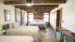 Una habitación rústica con dos camas, techo de madera, suelo de piedra y una mesa con cestas.