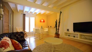 A living room with a leather sofa, a round table, a flat-screen TV, and a potted plant. - Spacious Apartment in Palma Old Town, Wifi, Air Conditioning, Fully Equipped (Palma)