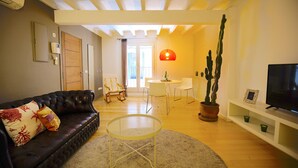 A living room with a dark leather sofa, a round glass coffee table, a white dining table with chairs, a potted cactus, and a flat-screen TV on a white stand. - Spacious Apartment in Palma Old Town, Wifi, Air Conditioning, Fully Equipped (Palma)