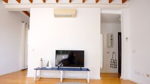 A living room with a flat-screen TV on a white bench, a grey rug, wooden flooring, and a ceiling fan.