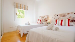 A hotel room with two beds, white bedding, striped curtains, and a window with a view of greenery.