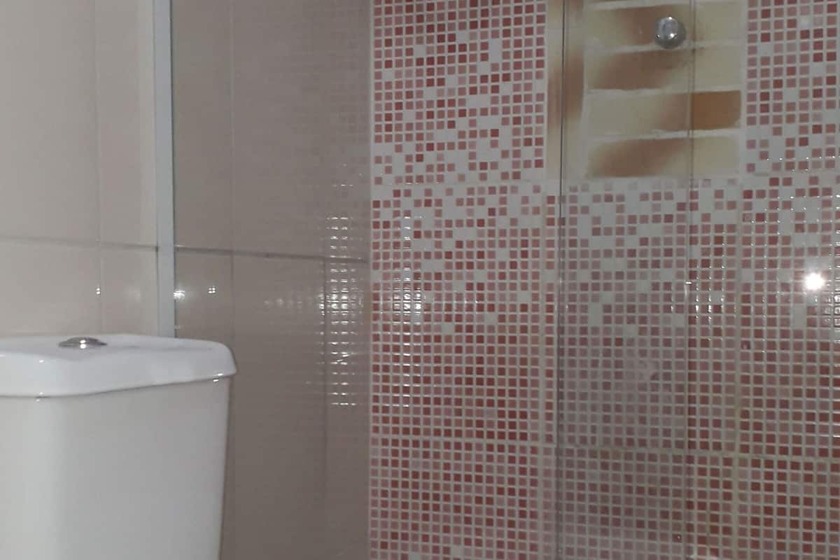 Une salle de bain comprenant des toilettes, un espace douche avec des carreaux de mosaïque et un mur carrelé.