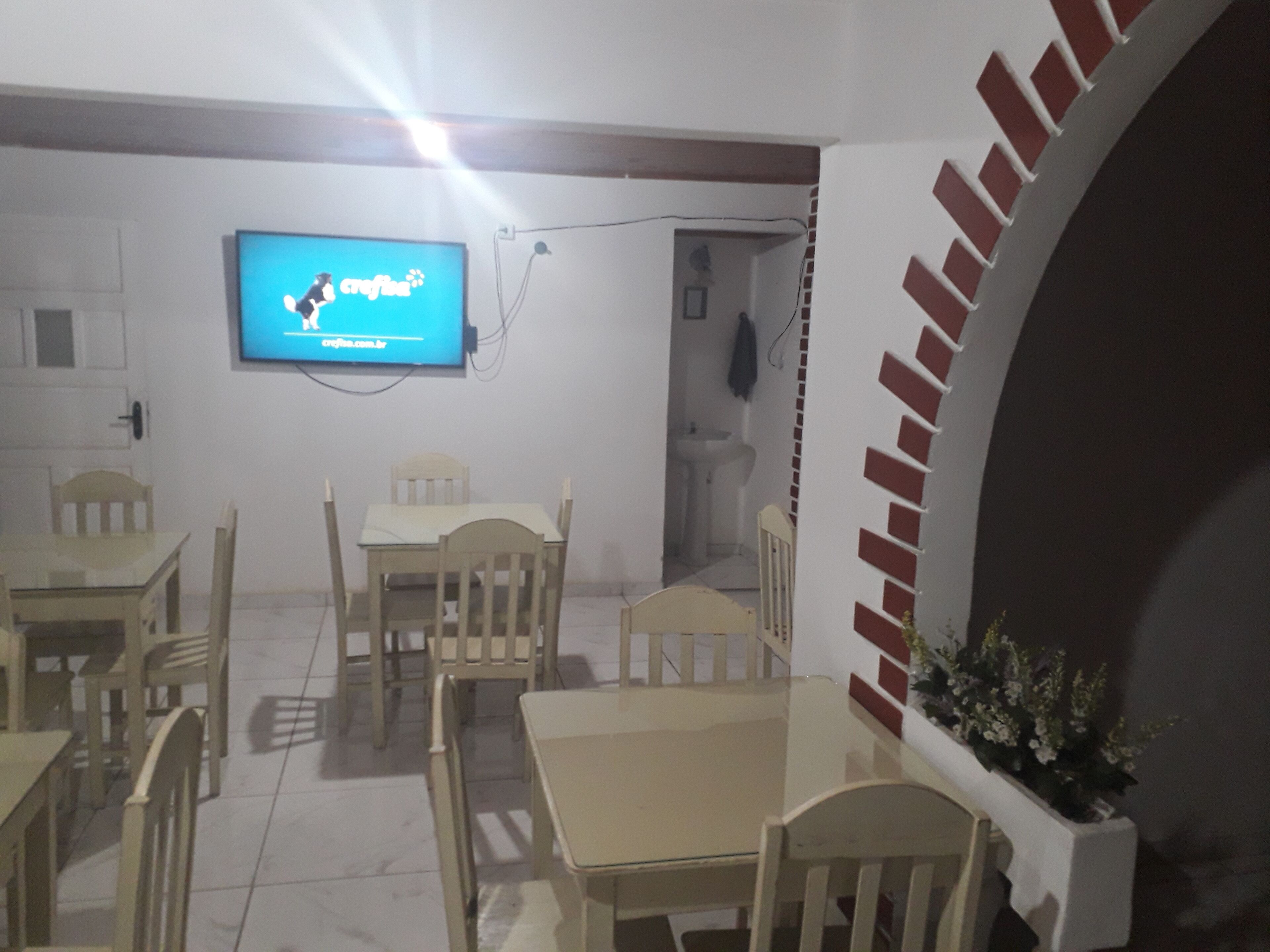A dining area with a television mounted on the wall displaying 'crafts.com.br'. There are wooden chairs and a table.