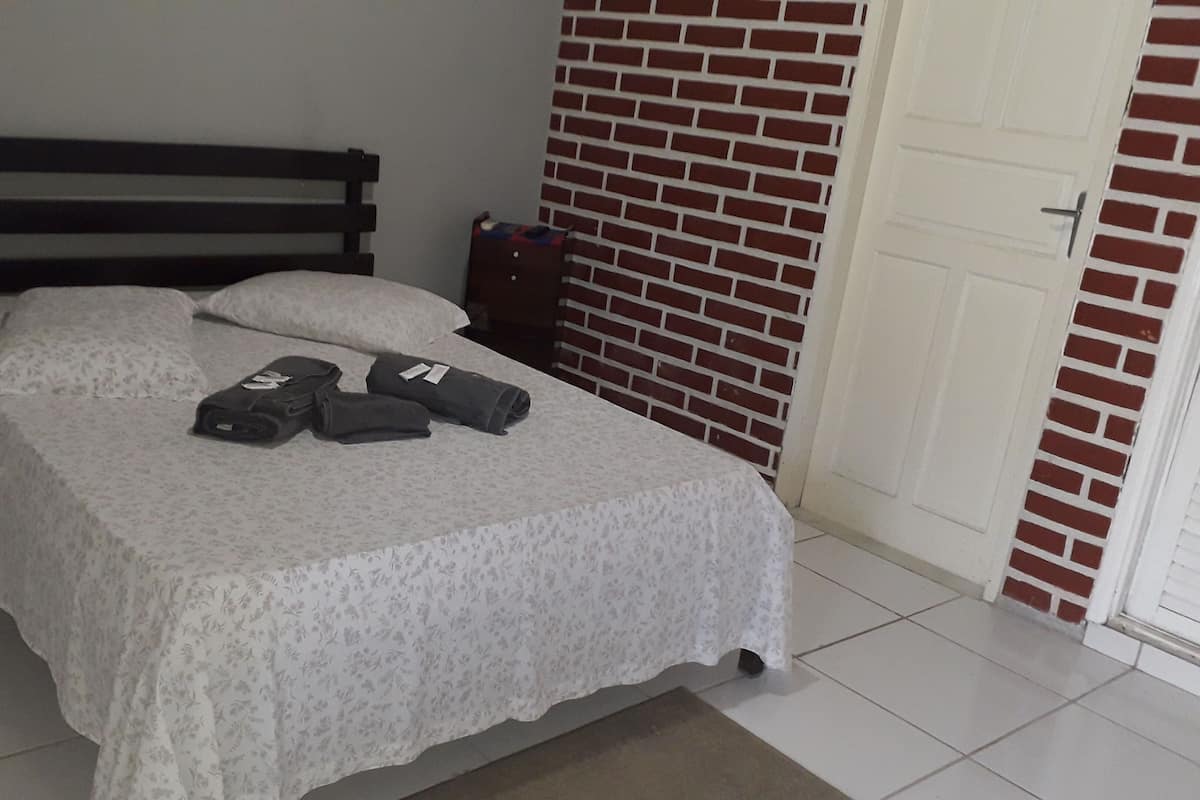 Un lit recouvert d’une courtepointe à motifs floraux blancs, avec une tête de lit en bois foncé et deux serviettes enroulées posées sur le lit.