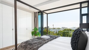 Ein modernes Schlafzimmer mit einem großen Bett, Blick auf die Stadt und einer Zimmerpflanze.