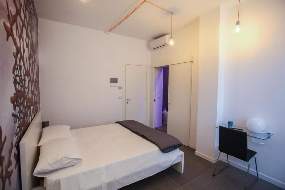 Ein Schlafzimmer mit einem Bett, einem Schreibtisch und einem Stuhl. Eine Tür führt zu einem Badezimmer.