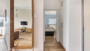 A modern hallway with wooden flooring, a visible bed in the background, and a TV in the living area. - Modern Space Footsteps from Sea Point Promenade (Cape Town)