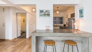 A modern kitchen with a concrete island, wooden stools, pendant lights, and artwork on the walls. - Modern Space Footsteps from Sea Point Promenade (Cape Town)