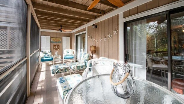 Una habitación soleada con una mesa de vidrio, sillas blancas acolchadas y un ventilador de techo.