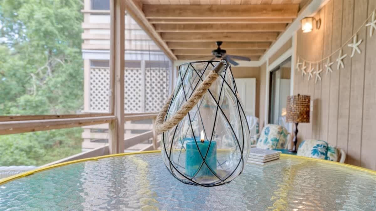 A glass table with a candle inside a wireframe lantern, a wooden ceiling, and a view of trees outside.