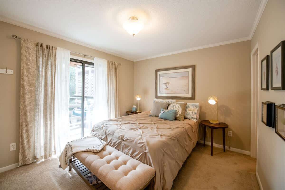 Ein Schlafzimmer mit einem großen Bett, einer Bank, zwei Nachttischen mit Lampen, einem Fenster mit Vorhängen und gerahmten Kunstwerken an der Wand.