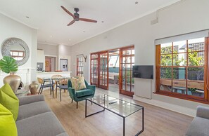 A spacious living area with a ceiling fan, a dining table with chairs, a sofa, and a large window with a view of greenery.