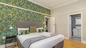A bedroom with a bed, nightstand, lamp, and a bathroom visible through an open door. - Gorgeous Green Point Home | 2 Bedroom | Patio (Cape Town)
