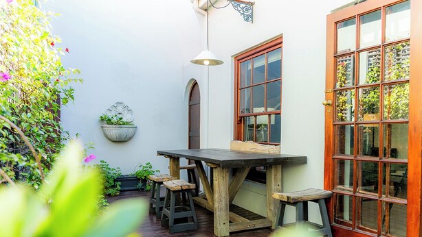 A wooden table with stools, a hanging planter, and a large window with a door. - Gorgeous Green Point Home | 2 Bedroom | Patio (Cape Town)