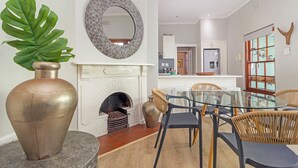 A dining area with a glass table, wicker chairs, a large vase, a fireplace, and a mirror on the wall. - Gorgeous Green Point Home | 2 Bedroom | Patio (Cape Town)
