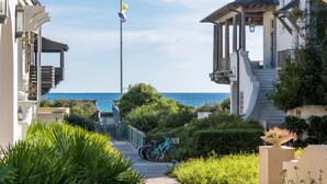 Una zona residencial costera con un paseo pavimentado, un asta con una bandera amarilla y vistas al mar.