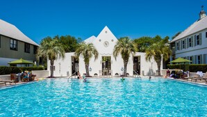 Una piscina con superficie de agua azul cristalina, rodeada de palmeras y un edificio con un reloj.