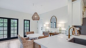 Cocina moderna con isla de mármol blanco, sillas de mimbre y un ventanal con vistas.