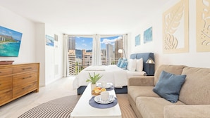 Habitación de hotel moderna con cama, sofá, mesa de desayuno y vista a la ciudad.