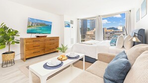 Habitación de hotel moderna con cama, sofá, mesa de comedor y vistas a la ciudad.