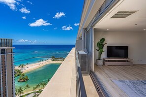 Un balcon avec une télévision, une plante et une vue sur l’océan et la plage.