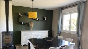 A dining area with a black table, white chairs, a white cabinet, a yellow pendant light, and a wood-burning stove.