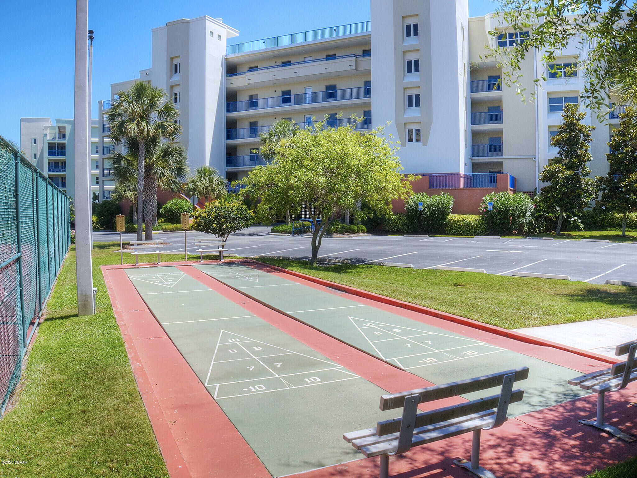 A courtyard with a shuffleboard court, benches, and a fence.