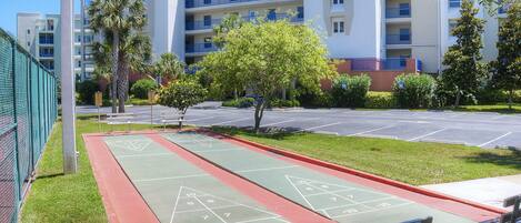A courtyard with a shuffleboard court, benches, and a fence.
