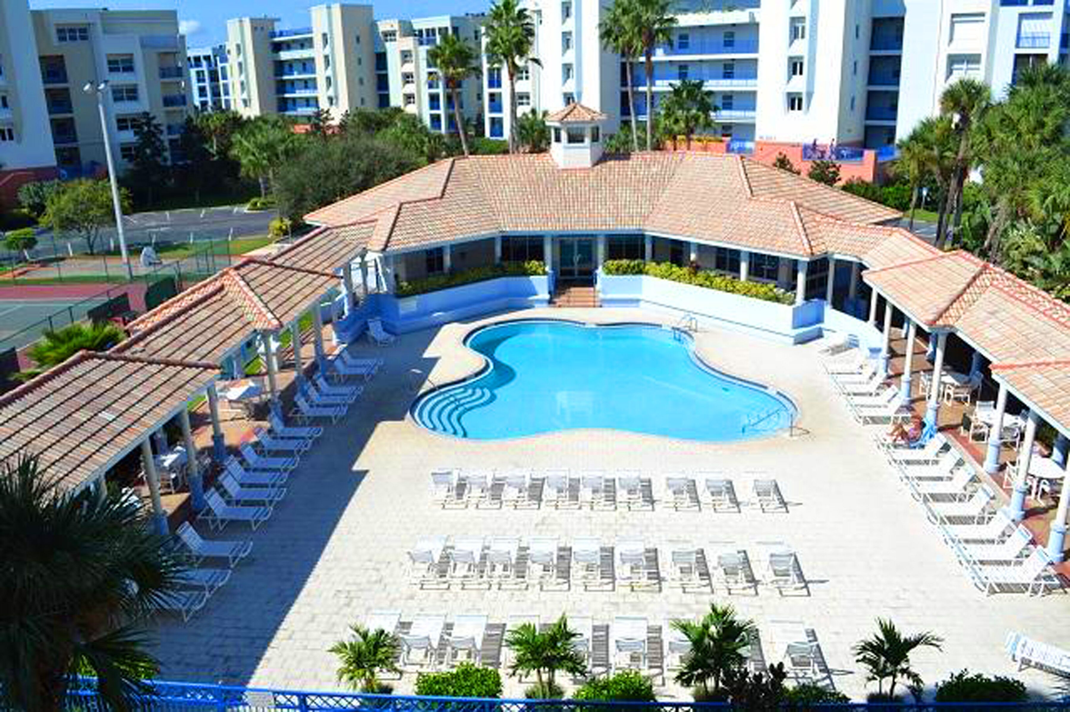 Un resort con piscina central, tumbonas y una zona de patio cubierta.