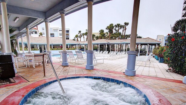 A hot tub with a metal ladder, surrounded by lounge chairs and a covered area with columns.