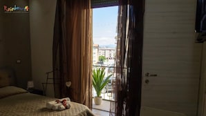 Habitación de hotel con cama, una planta en maceta y vistas a la calle a través de una ventana con cortinas.