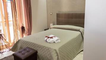 Habitación de hotel con una cama, una mesita de noche, una pequeña mesa y un ventanal con cortinas.