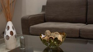 Un salón moderno con una mesa de centro de vidrio, un cuenco decorativo y un florero con cañas.