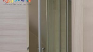 Un baño moderno con cabina de ducha de vidrio, una puerta de madera y un toallero visible.