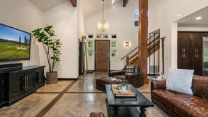 A spacious living room with leather sofas, a flat-screen TV, and a large plant.