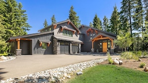 A modern two-story house with a stone foundation, large windows, and a stone pathway leading to the entrance.