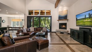 A spacious living room with a large brown leather sofa, a fireplace, a television, and a dining area with a table and chairs.