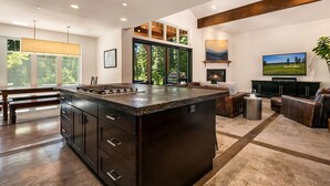 A modern kitchen with a large island, a dining area with a bench, and a living room with a fireplace and television.