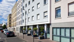 Un hotel de varios pisos con fachada moderna, amplias ventanas y una fila de macetas a lo largo de la acera.