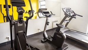 Un gimnasio con diversas máquinas de ejercicio, incluyendo elípticas y una cinta de correr, frente a una pared amarilla.