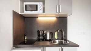 Una kitchenette compacta con microondas, cafetera, hervidor y pileta.